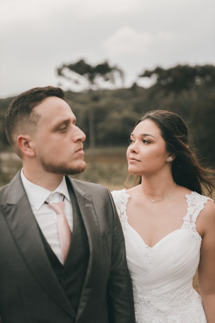 A newlywed couple poses elegantly outdoors in wedding attire, captured in a serene countryside.
