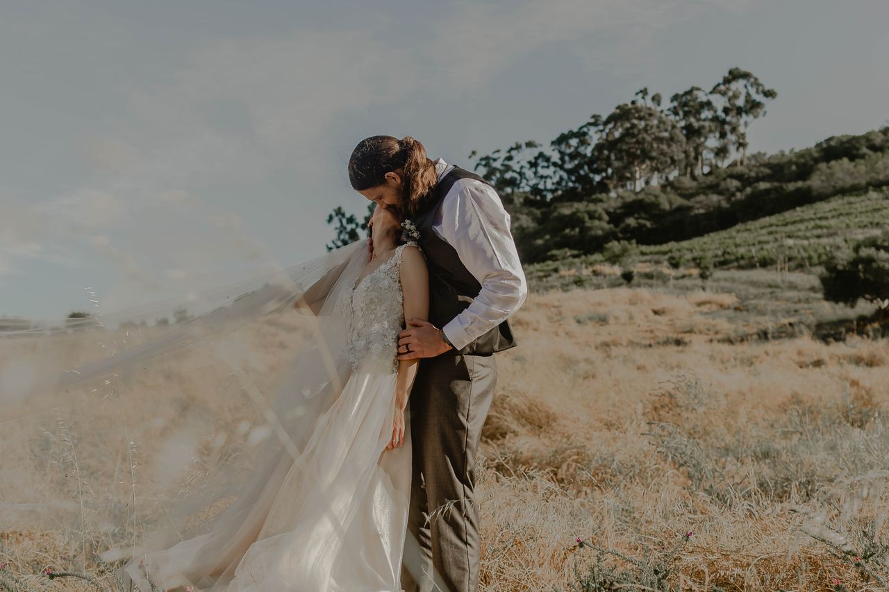 A bride and groom share a sweet moment in a tranquil, sunlit field.