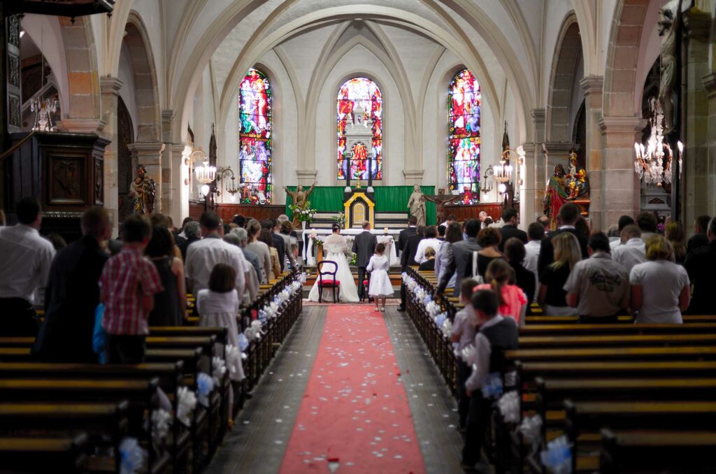 Mariés debout au bout de l'allée centrale de l'église entourés des bancs des invités