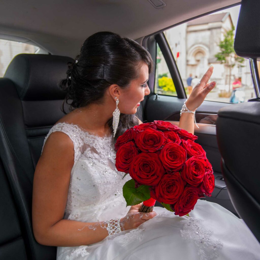 Mariée saluant ses invités depuis une voiture avec un bouquet de roses
