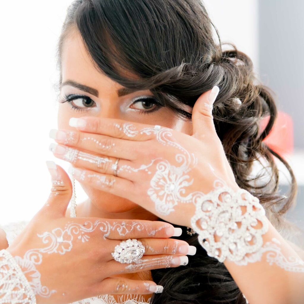 Future mariée se regardant dans un miroir, le visage partiellement caché par ses mains maquillées