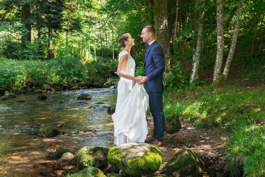 Couple de mariés se tenant la main dans une forêt près d'un cours d'eau