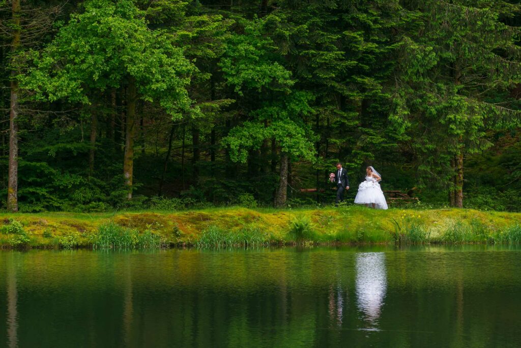 Couple de mariés marchant au bord d'un étang avec leur reflet dans l'eau
