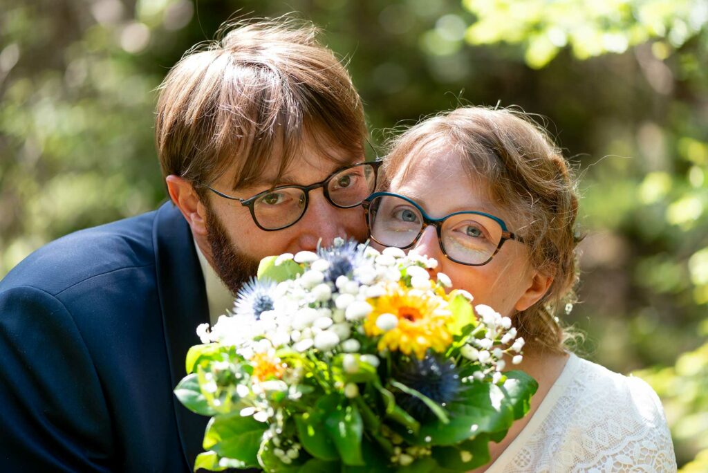 Yeux des mariés visibles derrière un bouquet de fleurs dans un cadre naturel